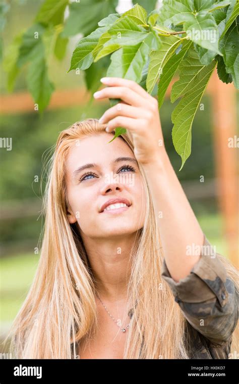 Blond Beautiful Girl Loving Nature Outdoors As She Touches A Green Leaf Respecting Its Spirit