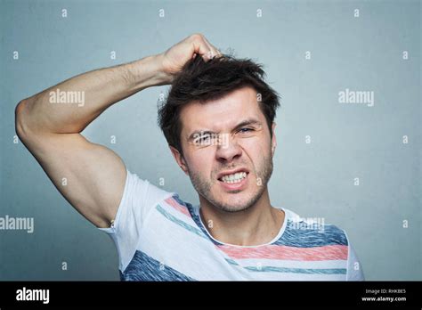 Portrait Of Frustrated Young Man Pulling His Hair On Gray Wall