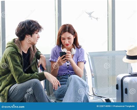 Asian Young Traveler Lover Couple Siting On Terminal Chair Seat With Luggage Suitcase Having