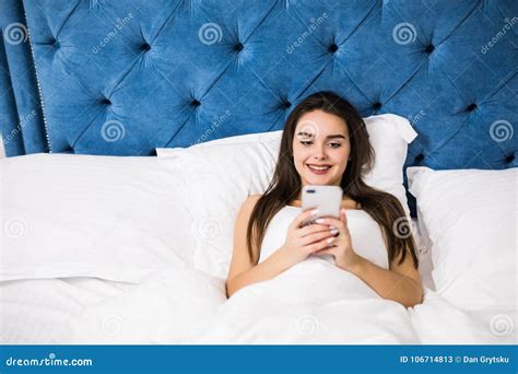Happy Young Woman Lying In Bed And Texting On Smartphone At Home