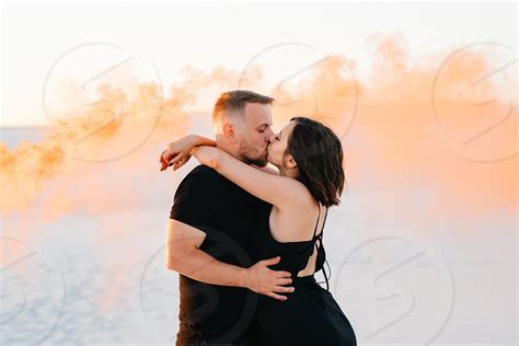 Guy And A Girl In Black Clothes Hug And Run On The White Sand With Orange Smoke By Andrii