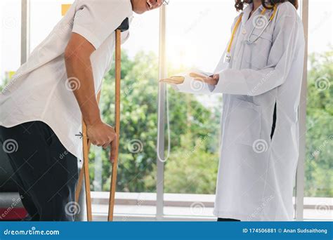 Physical Female Doctor Helping Patient With Crutches In Hospital Office