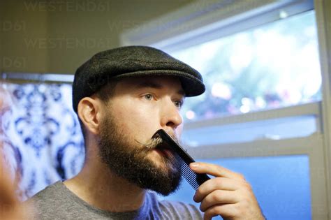 Man Combing Mustache While Looking Away At Home Stock Photo