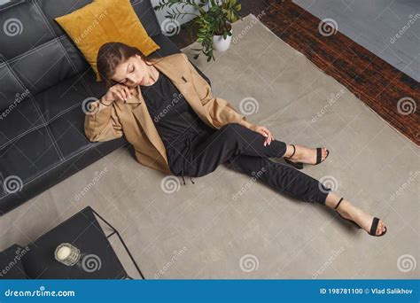 Stylishly Dressed Young Caucasian Woman In Beige Blazer And Black Pants Sitting On The Floor At