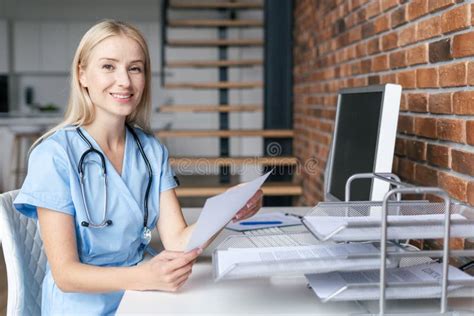 Happy Nurse In Medical Uniform Sitting In Office With Documents Stock