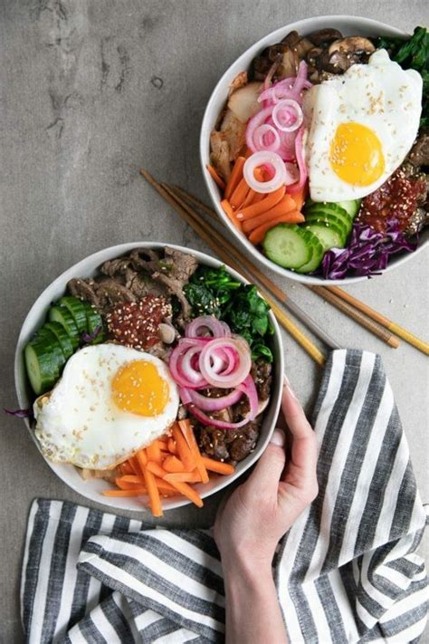 Two Bowls Filled With Meat And Vegetables Next To Chopsticks On A Table Top
