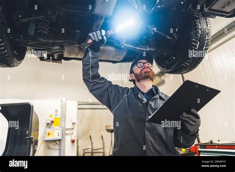 Mechanic With A Clipboard Inspecting The Car Chassis Of A Lifted Car