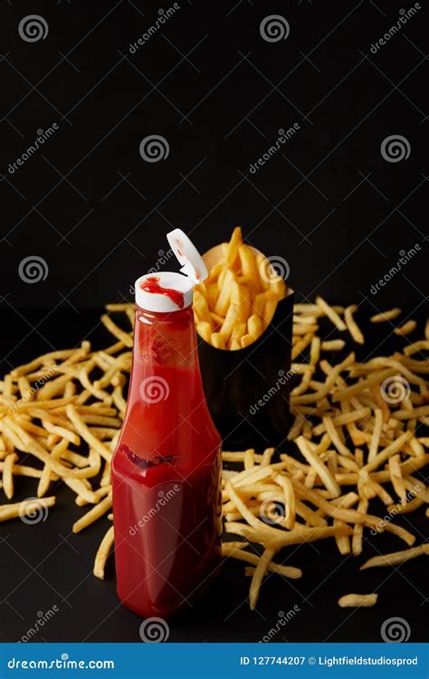 Bottle Of Ketchup With Messy French Fries On Black Surface Isolated On