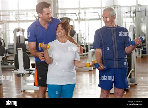 Handsome Male Trainer Instructing Senior Woman In Gym Elderly People