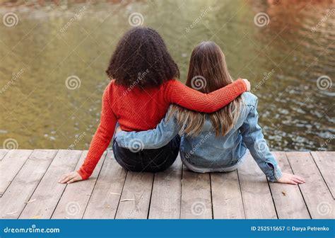 Back View Of Two Happy Multiracial Girlfriends Sitting Near River With Happiness Two Best