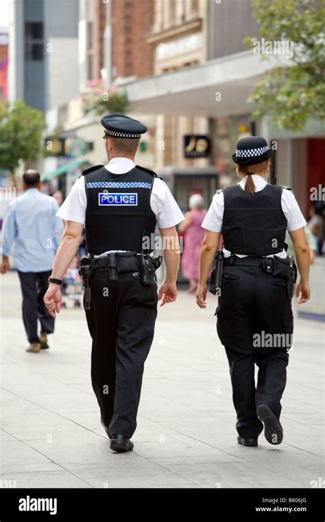 Back View Of Two Police Officers Male And Female Walking Down The
