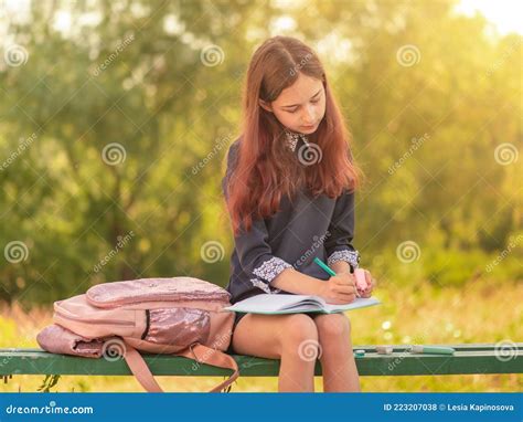 Girl Teenager Schoolgirl Writes In A Notebook Sitting On A Bench Stock