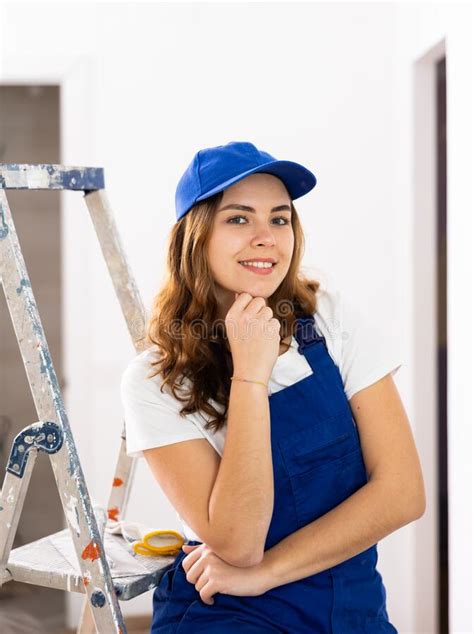 Portrait Of Contented Young Female Builder In Blue Overalls During The