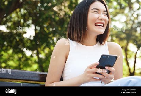Happy Asian Girl Sitting On Bench And Using Mobile Phone Girl Resting