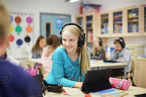 Smiling Girl Wearing Headphones While Using Digital Table In Classroom