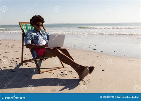 Man Using Laptop While Relaxing In A Beach Chair On The Beach Stock