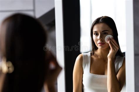 portrait of beautiful woman in bathrobe and with towel on her head cleaning her face with sponge