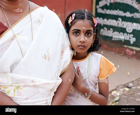 A Young Girl Peeps Out From Behind Her Mother In A Village South Of