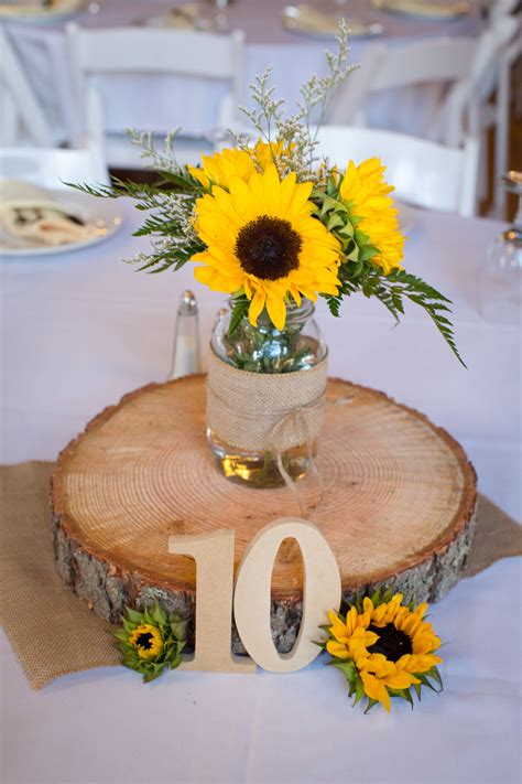 Sunflowers And Greenery Are Arranged In A Vase On Top Of A Wood Slice