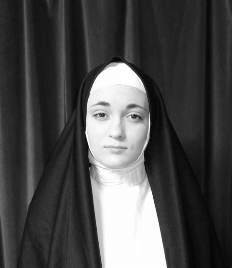 A Nun Standing In Front Of Black Curtains With Her Head Turned To The
