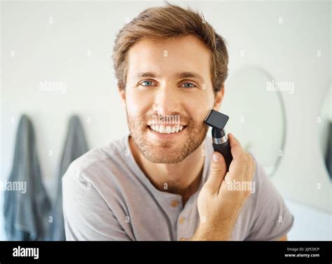 one handsome man shaving his face hair in a bathroom at home caucasian male using a shaver