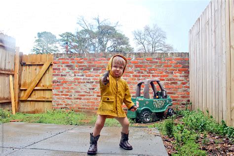 Toddler In Raincoat And Boots Making Silly Face Outside Del