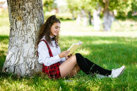 Beautiful European Schoolgirl Sits In A Park Near A Tree On The Green