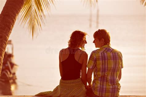 Young Couple Sit Together Under A Palm Tree And Looking Toward S Stock