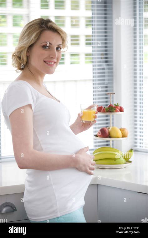 pregnant female fair hair tied at the back wearing a white t shirt and blue trousers standing