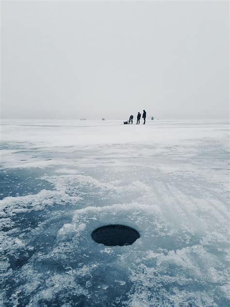 Fishermen Drilling Ice Fishing Holes On Frozen Lake By Stocksy