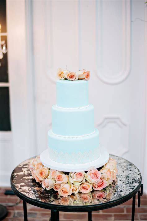 Light Blue Wedding Cake With Lace Accents And Topped In Peach Roses