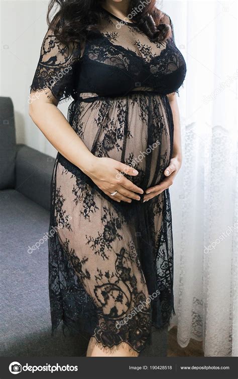 A Pregnant Girl Stands By The Window Dressed In A Transparent Dr