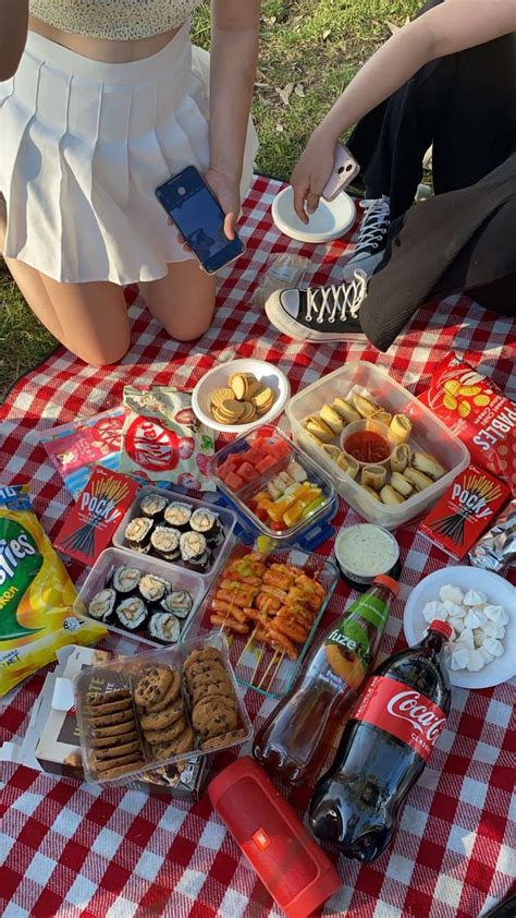 Two People Sitting At A Picnic Table With Food And Drinks On It One