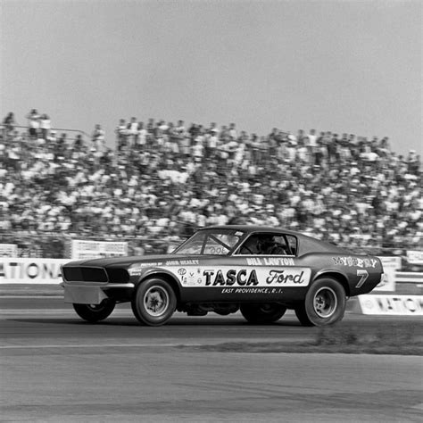 A Black And White Photo Of A Race Car Going Around A Track In Front Of