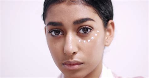 Applying eye cream in small dots under eyes and gently ...