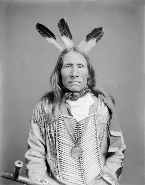 An Old Black And White Photo Of A Native American Man With Feathers On His Head