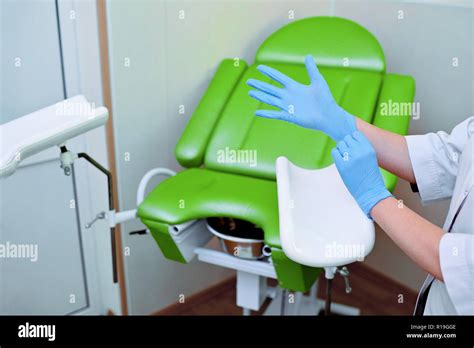 frauenarzt setzt auf handschuhe auf dem hintergrund einer gynäkologischen stuhl Ärztliche