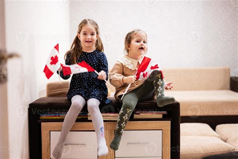 Duas Irmãs Estão Sentadas Em Um Sofá Em Casa Com Bandeiras Canadenses Nas Mãos Canadá Crianças