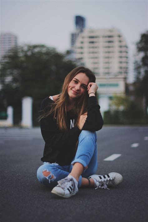woman smiling while sitting on road with hand resting on top of her knee fashion photography