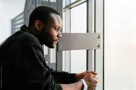 Young Black Man With Pensive Expression Looking Out Window By Stocksy