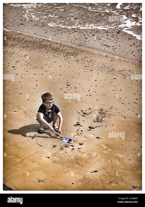 Boy Digging On A Sandy British Beach Stock Photo Alamy