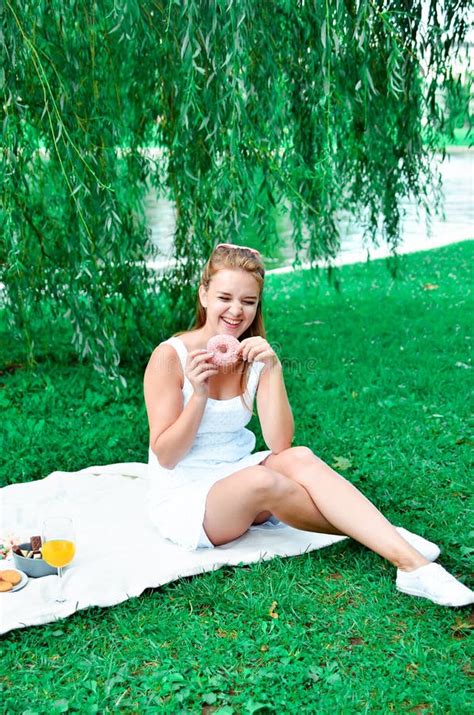 Young Girl With Hair Bow In A White Dress And Sneakers Eating Sweets And Drink Orange Juice