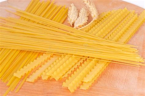 Different Uncooked Long Pasta And Wheat Ears On Wooden Board Stock