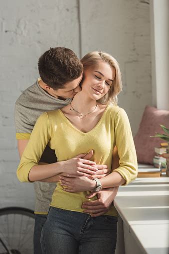 Boyfriend Hugging Girlfriend And Kissing Her Neck At Home Stock Photo