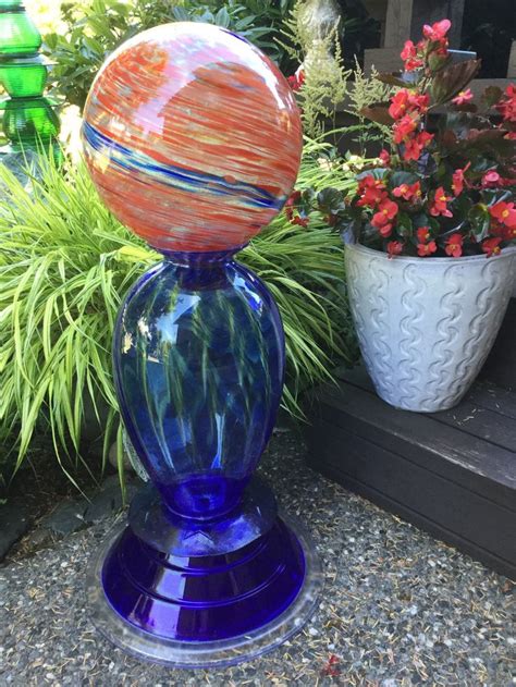 A Blue Vase With An Orange Ball On It Sitting In Front Of Some Flowers