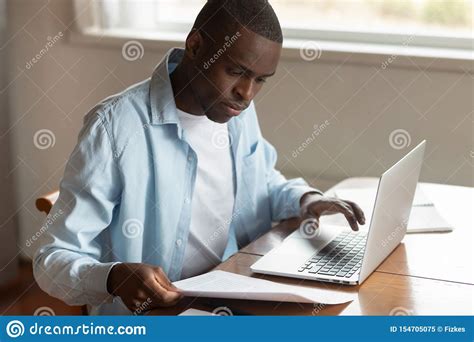 African Man Sitting At Table Paying Household Bills Using Laptop Stock