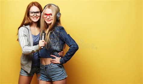 Dos Chicas J Venes Que Cantan Sobre Fondo Amarillo Foto De Archivo