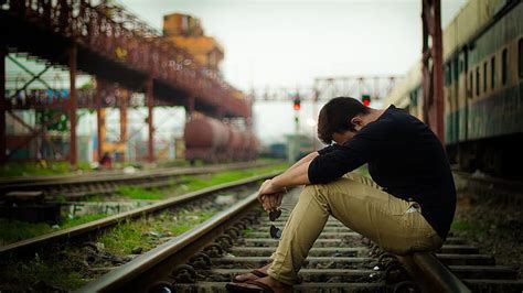 Sad Looking Man Is Sitting Alone On Railway Track Wearing Black Brown