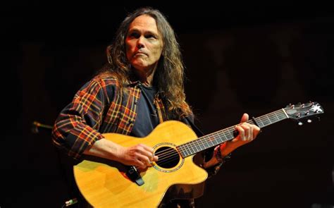 a man with long hair playing an acoustic guitar