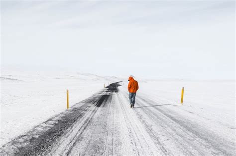 A Lone Man Walking On A Snowy Road Surrounded By Snow Covered Fields